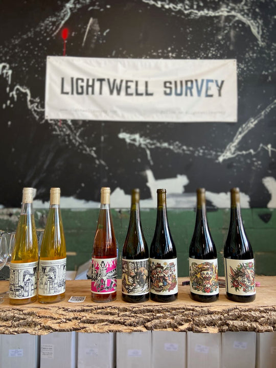 Array of Lightwell Survey wine bottles with sign in background 