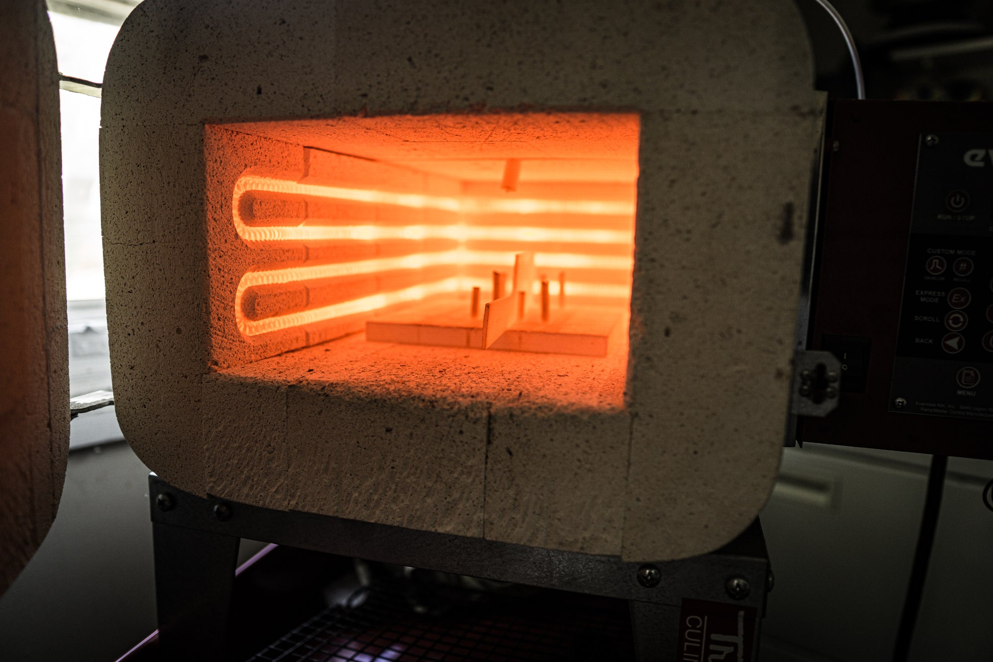 Open door on heat treat kiln with heating elements on with knife on ceramic rack.