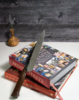 A 9-inch chef knife with a wooden handle, placed on top of two cookbooks, with a dark wooden background.
