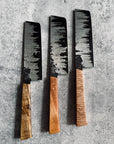 Three Japanese style vegetable knives with wooden handles and stainless steel blades, laid out on a textured grey surface.