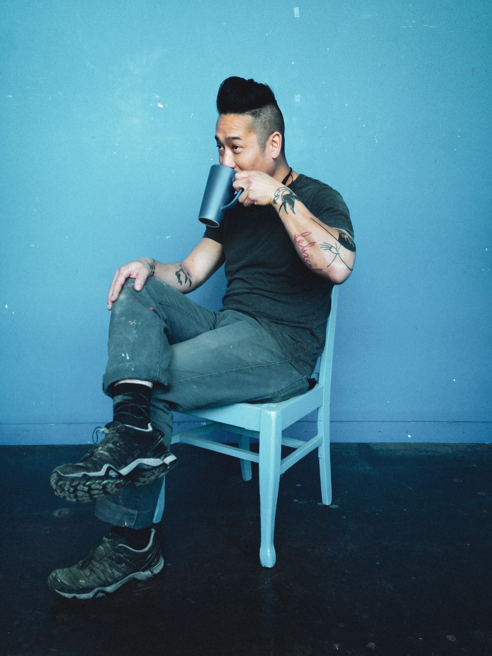 Dustworks Vu Portrait seated on blue chair in blue room drinking out of blue coffee mug wearing blue pants and blue t-shirt
